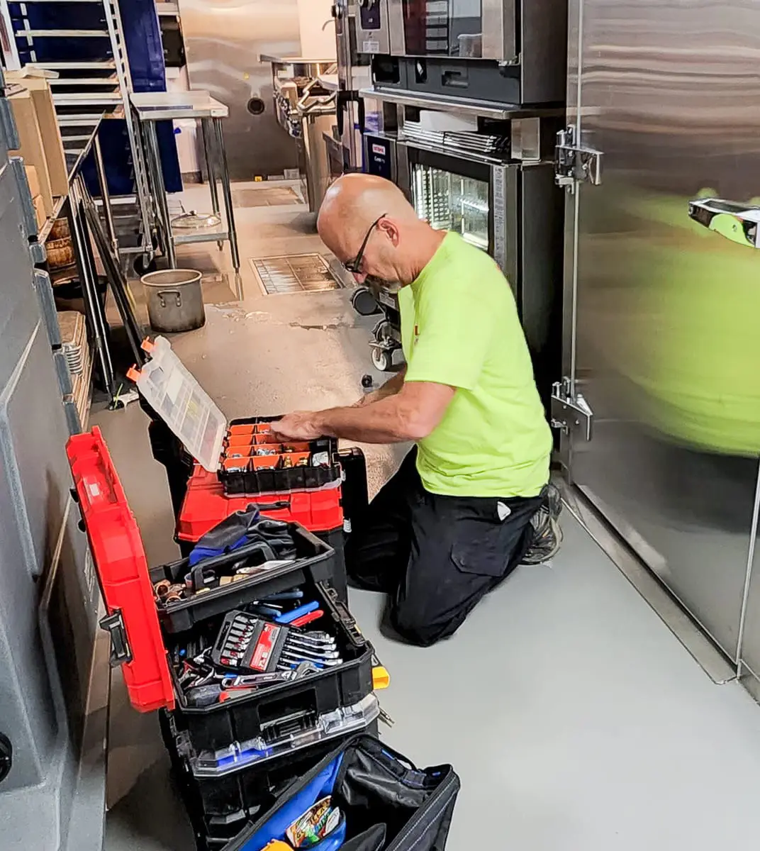 Commercial Appliance Technician kneeling on ground with several open tool boxes in front of him.