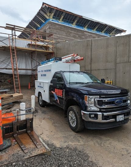 A dark blue Ford pick-up truck with a white service body and "PRIDECAS" decal parked at a construction site. In the background, the niagara welcome center building with an unfinished roof and scaffolding is visible.