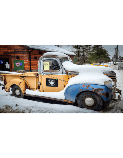 Old time truck outside a building made of wood logs with sides on it