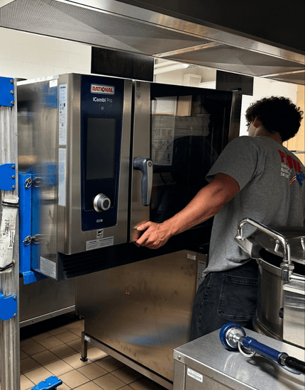 technician holding a large commercial oven, assisted by a hoisting machine