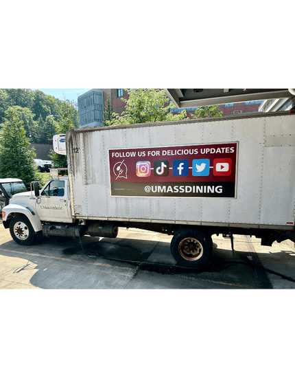 White delivery truck with UMass Dining social media banner displaying Instagram, Twitter and YouTube icons and handle @UMASSDINING parked on campus