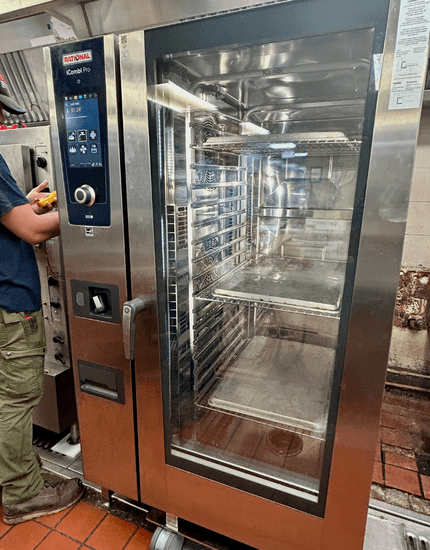 Technician operating large stainless steel commercial convection oven with glass door and digital control panel in professional kitchen setting