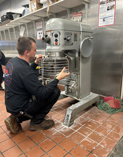 technician kneels in front of a commercial grade kitchen mixer screwing on a safe guard grate
